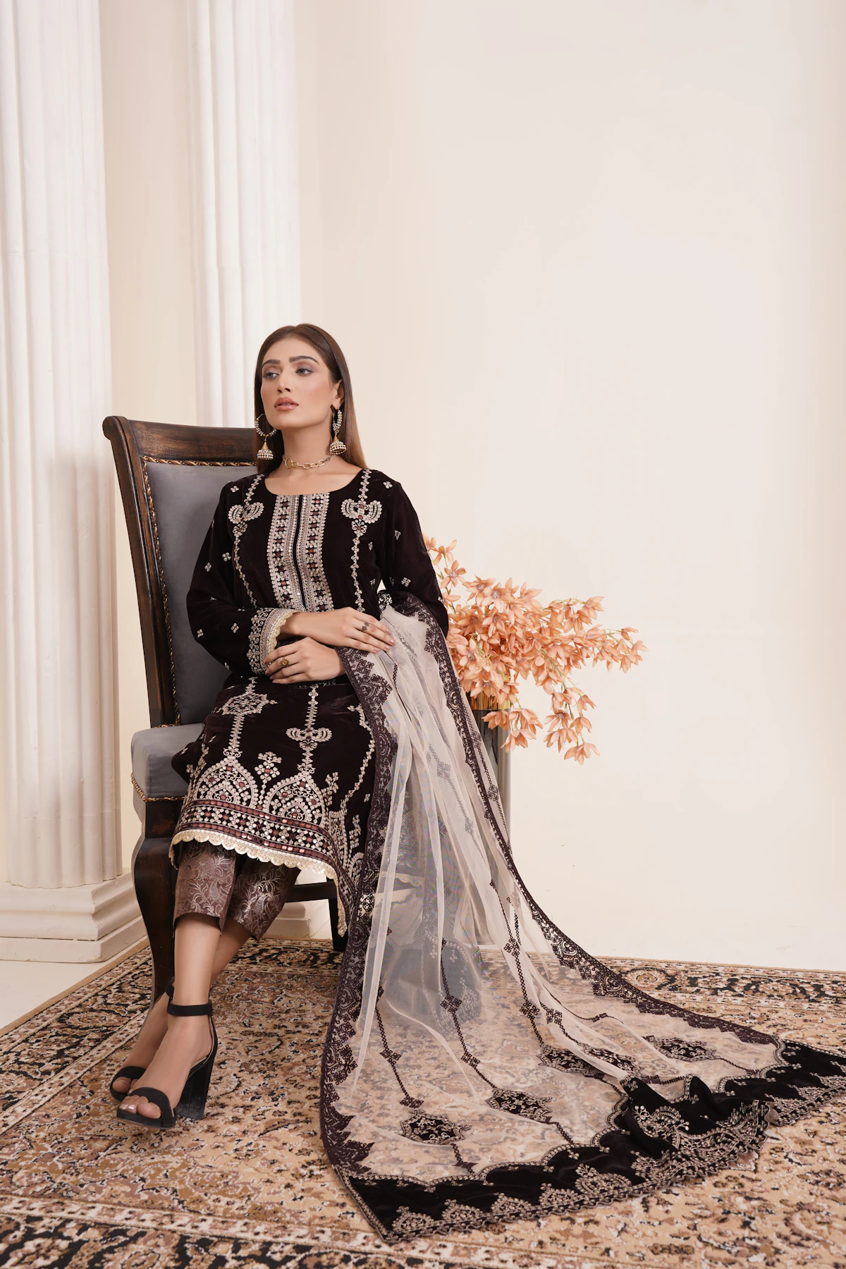 A woman seated in a black velvet formal with silver embroidery and a grey embroidered net shawl.