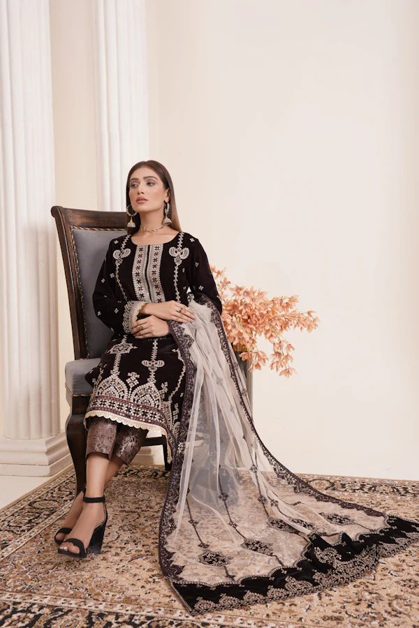 A woman seated in a black velvet formal with silver embroidery and a grey embroidered net shawl.