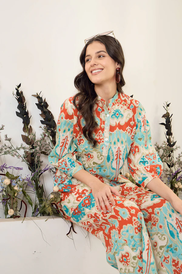 A smiling woman in a blue, orange and cream ikat print shirt and matching trousers.