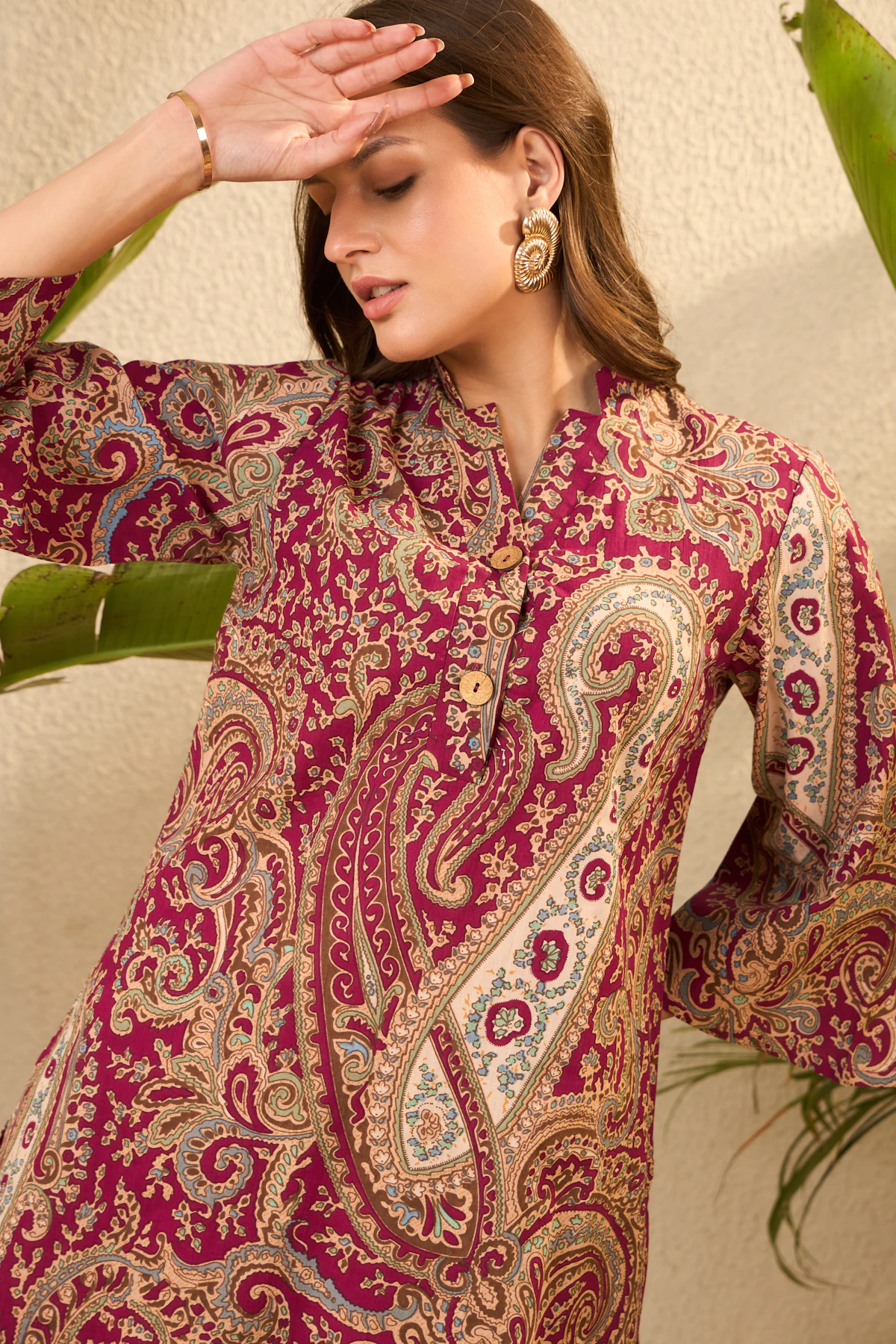 A woman in a maroon kurta with a large gold and cream paisley print and bell sleeves.