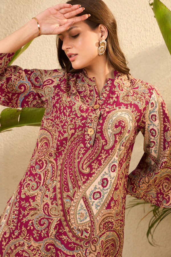 A woman in a maroon kurta with a large gold and cream paisley print and bell sleeves.