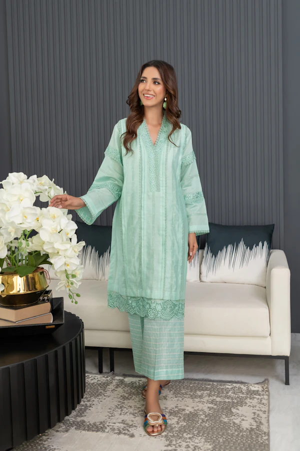 A woman in a mint green lawn suit with schiffli embroidery and wide trousers, standing in a white living room.