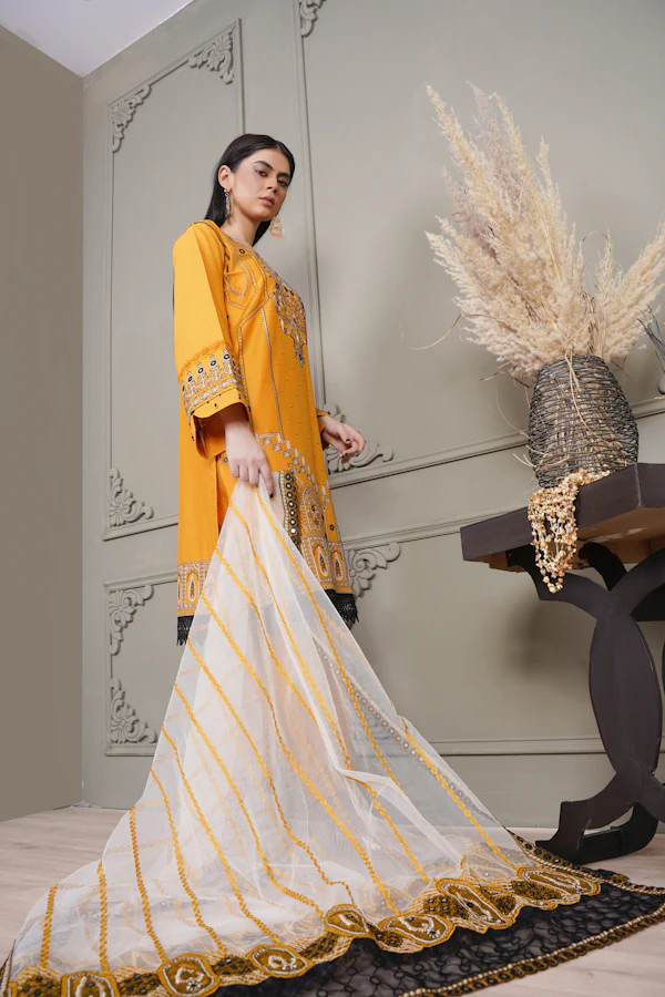 A woman in a mustard yellow kurta holding a long white dupatta with gold stripes.